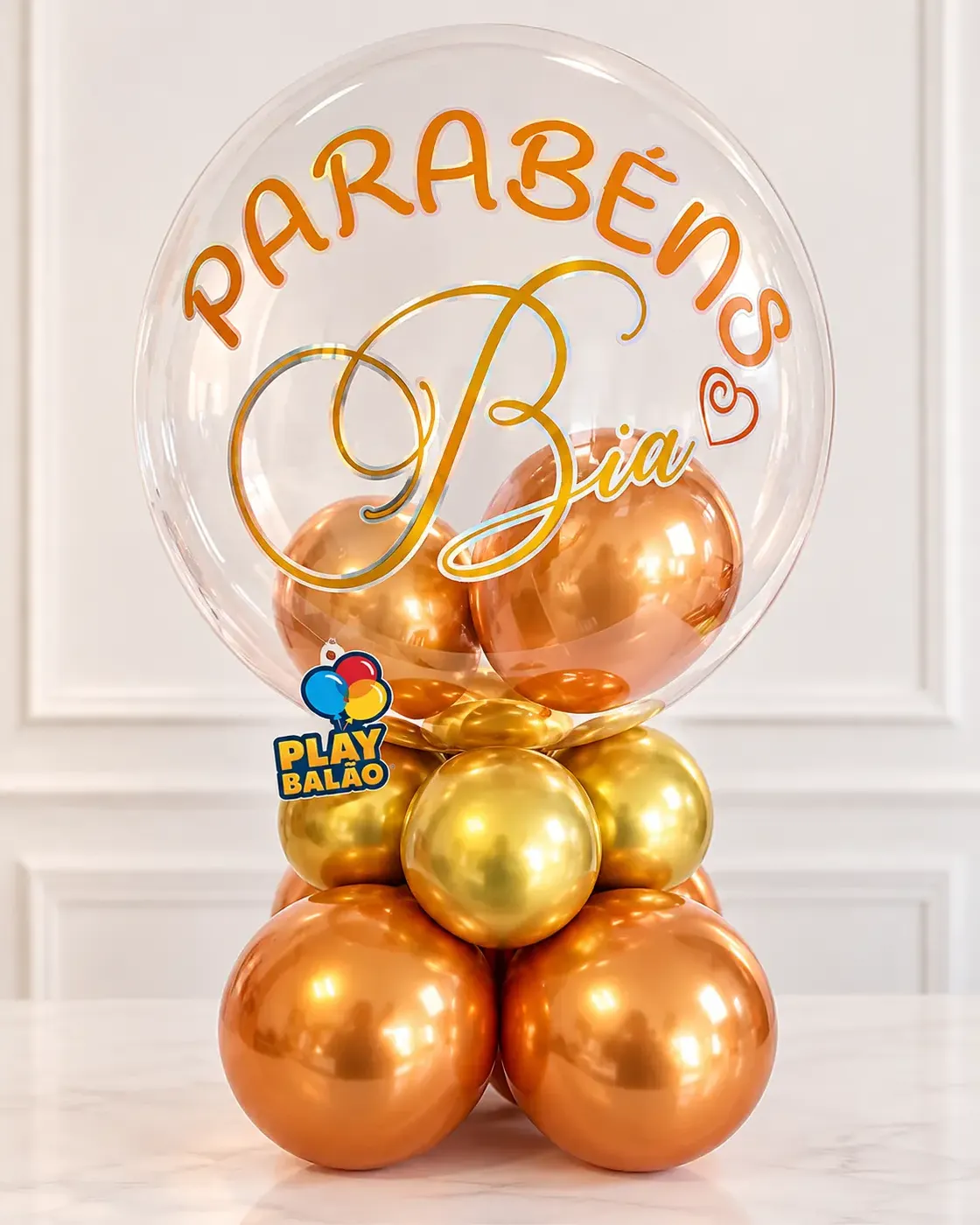 Balão bubble personalizado com nome sobre arranjo cobre e dourado